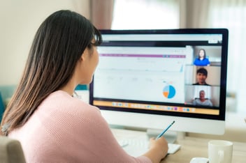 Woman attending a virtual conference, taking notes while speakers present on her computer screen