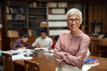 A professor smiles in a library after her employer determined how to improve faculty leave management.
