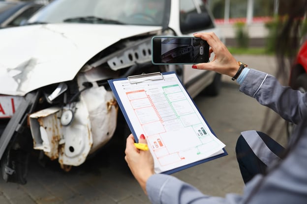 Person holding a form while taking a photo of a damaged car