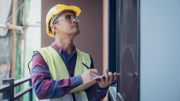 Construction worker examines wall while taking notes