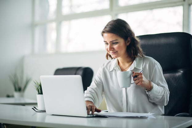 Manager holding a cup of coffee while typing