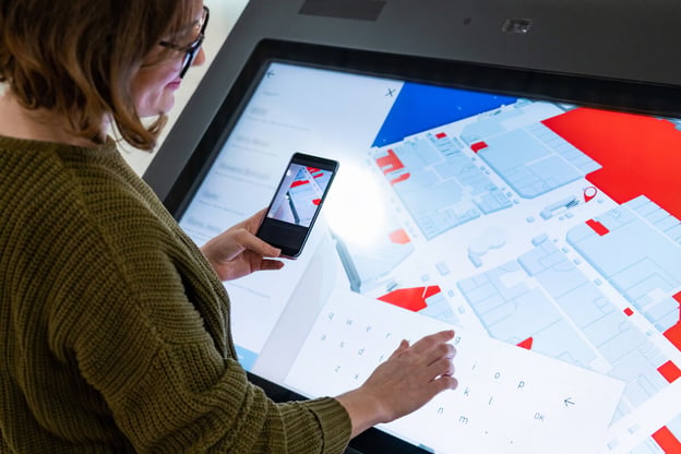 Digitization of customer experience: woman holding her mobile phone while using a digital building directory