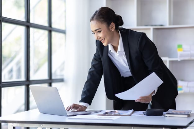 Manager using a laptop while holding a piece of paper