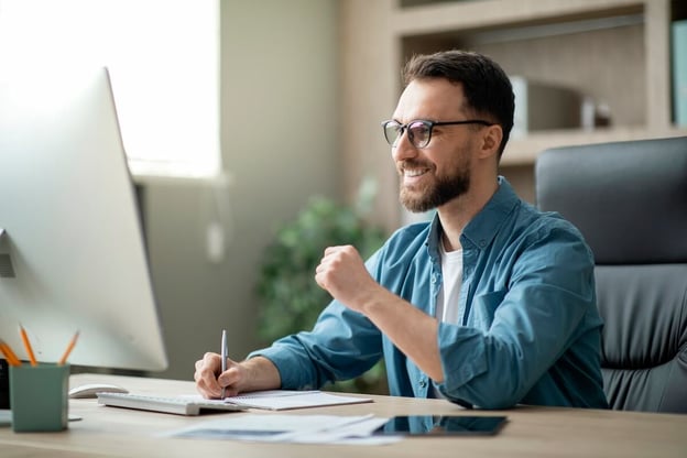 Entrepreneur writing in a notebook while looking at his computer