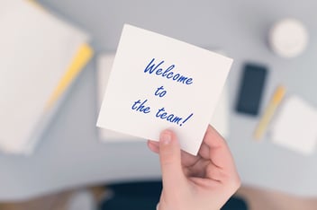 Onboarding documents: person holding a note with 'Welcome to the team!' written on it
