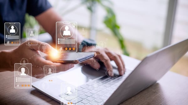 Benefits of AI in HR: person using a phone and a laptop with holographic profile icons