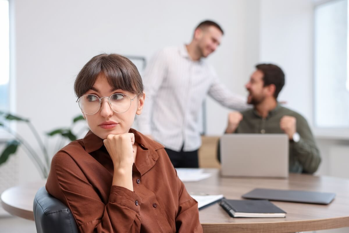 Managing employee relationships: employee looking away while her 2 colleagues are talking in the background