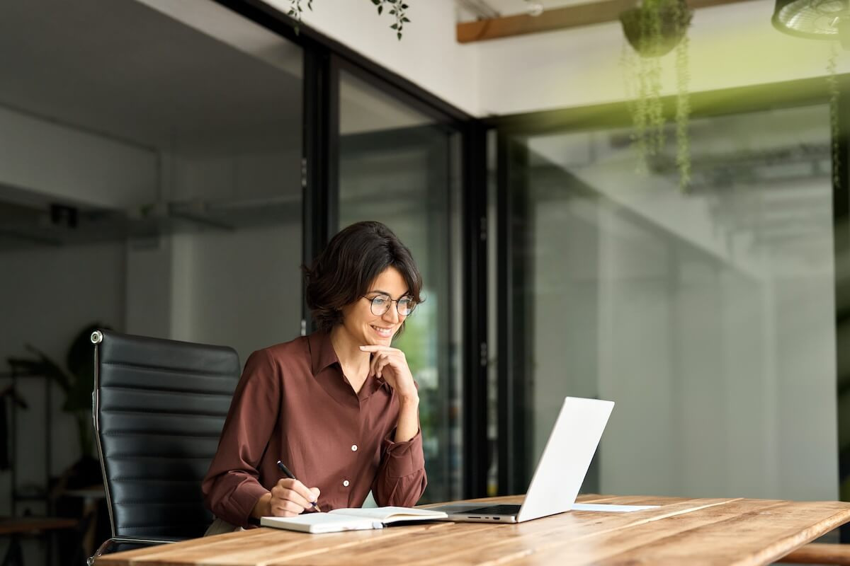 Business case HR technology: HR manager writing in a notebook while looking at her laptop