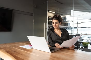 HR team member looking at a laptop while holding some documents