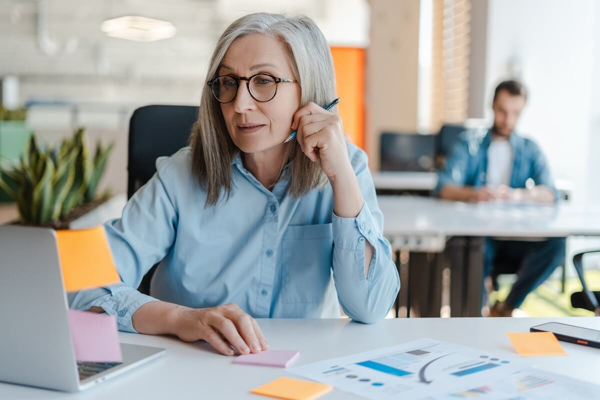 Automated leave management system: senior employee looking at her laptop while holding a pen