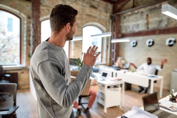 Automate leave management: employee waving to his colleague while holding a small box