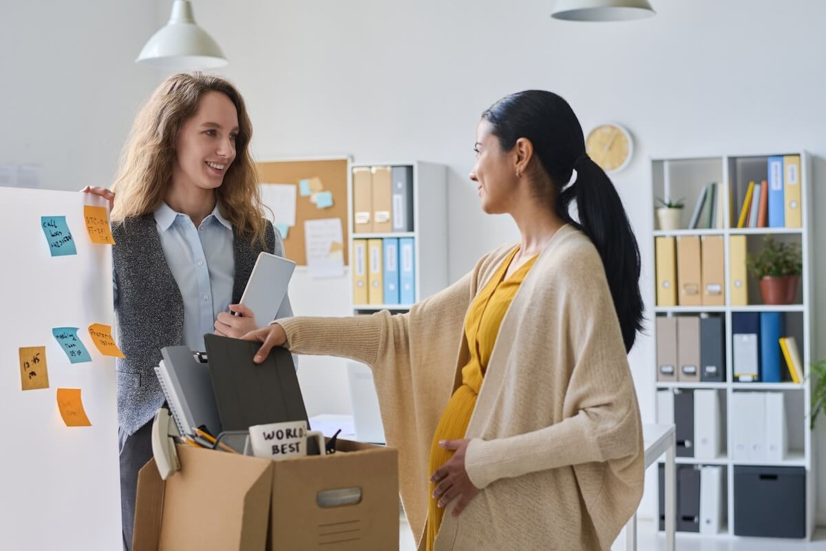 FMLA Maine: pregnant employee packing her belongings while talking to a colleague