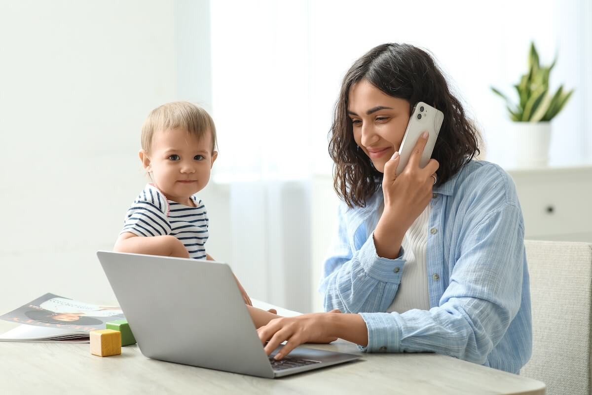 Mom talking on the phone and using a laptop while taking care of her baby